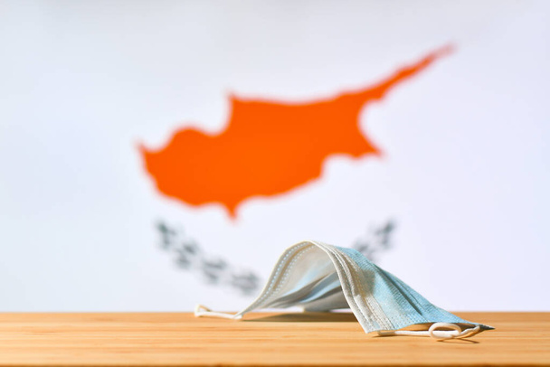 Na stole leży maska medyczna na tle flagi Cypru. Koncepcja systemu obowiązkowej maski dla mieszkańców kraju i turystów na Cyprze podczas pandemii. - Zdjęcie, obraz