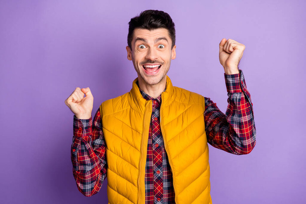 Photo of shocked lucky guy dressed yellow vest big eyes open mouth rising fists isolated purple color background - Foto, Bild