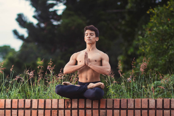 Young Latino man meditating and practicing yoga in the forest - Photo, Image