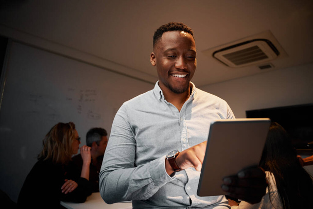 Портрет успешного молодого африканского бизнесмена, использующего свой цифровой планшет во время встречи - Фото, изображение
