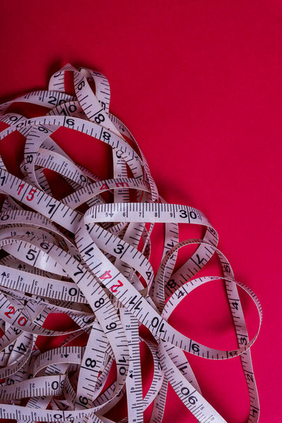 Measuring tape rolled out randomly on red background. - Photo, Image