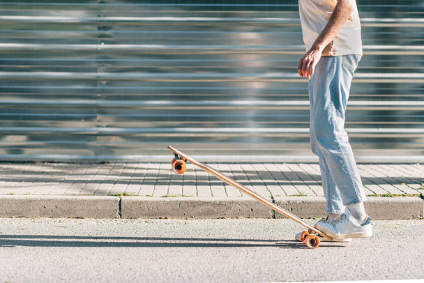 uomo irriconoscibile con abiti casual sollevare uno skateboard con i piedi - Foto, immagini
