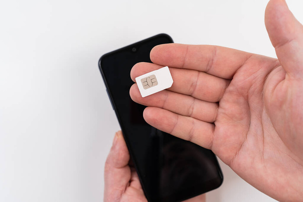 egy férfi kezében van egy SIM-kártya egy fekete okostelefon közelében - Fotó, kép