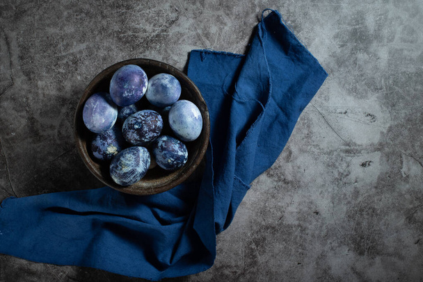 a tojásokat áfonyával festik márványminta formájában. kék húsvéti tojás fekszik egy agyag tál egy kő háttér. - Fotó, kép