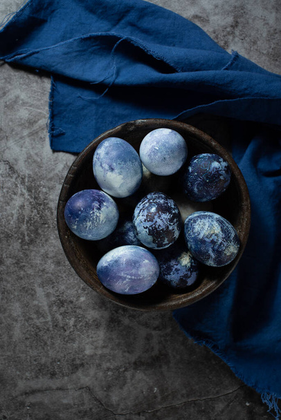 eggs are painted with blueberries in the form of a marble pattern. blue Easter eggs lie in a clay bowl on a stone background. - Foto, Imagen