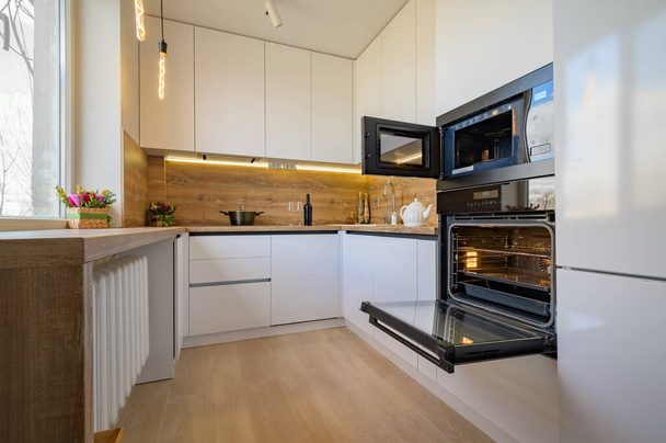 Moderne witte en beige houten keuken interieur met oven geopend - Foto, afbeelding