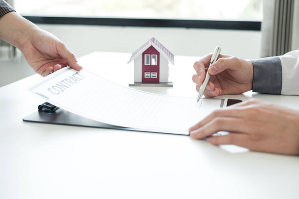 Immobilienmakler bieten eine Hausratversicherung an und schließen den Verkauf sofort ab, nachdem der Kunde einen Kaufvertrag im Rahmen einer formellen Vereinbarung unterzeichnet hat. Immobilien Eigenheimversicherungskonzept. - Foto, Bild