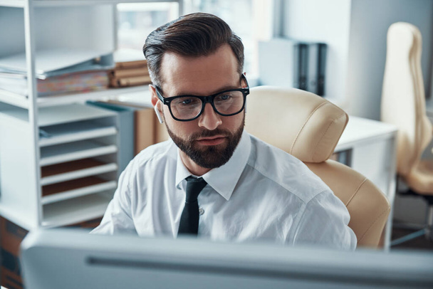 Concentrated young man in shirt and tie working on computer while sitting in the office - Photo, image