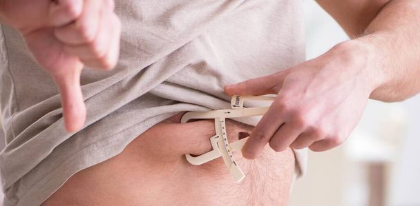 Чоловік вимірює жир тіла за допомогою штангенциркулів
 - Фото, зображення