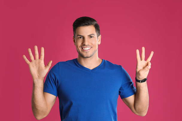 Hombre mostrando el número ocho con sus manos sobre fondo rosa - Foto, Imagen