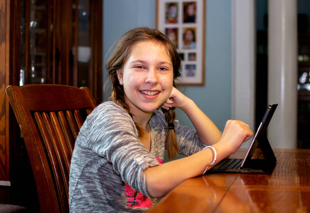 Gülümseyen kız, karantina sırasında derslerine çalışırken okul bilgisayarıyla poz veriyor. - Fotoğraf, Görsel