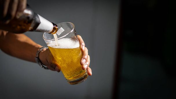 Eine Nahaufnahme der Flasche und des Bierkrugs in der Hand und das Bier in das Glas gießen. - Foto, Bild