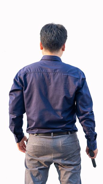A young Asian man in a blue shirt holds a gun in his hand. White background. - Photo, Image