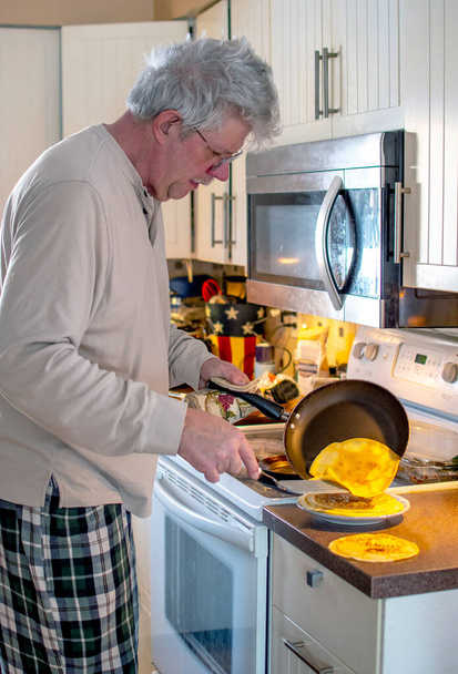 idősebb férfi csinál palacsintát reggelire az otthoni konyhában villásreggelire - Fotó, kép