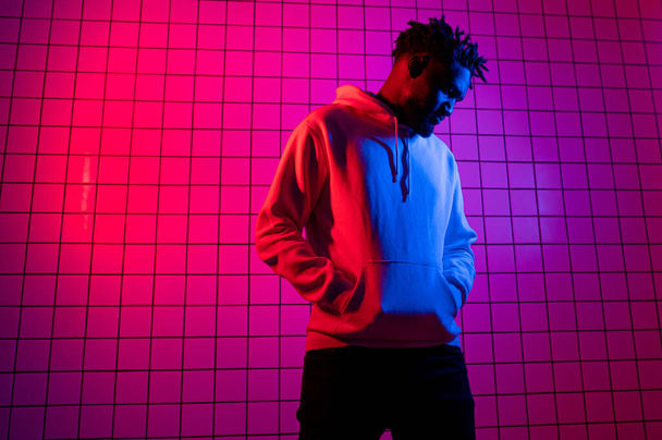 Portrait of an African American man in a hoodie on a neon background. Red-blue background. - Фото, зображення