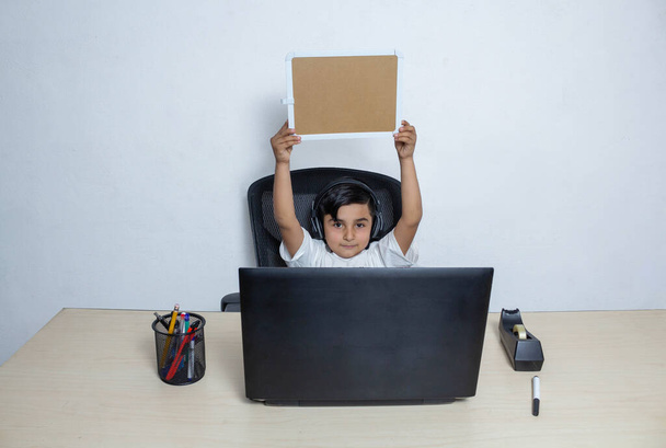 niño delante de la computadora portátil levantamiento y mostrando pequeña pizarra vacía. Estudiante mexicano - Foto, imagen