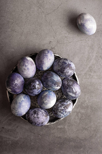 mramorová velikonoční vajíčka na tmavém pozadí, ručně malovaná přírodními borůvkami, leží v hliněném šálku na kamenném stole. Koncept přípravy Velikonoc. - Fotografie, Obrázek