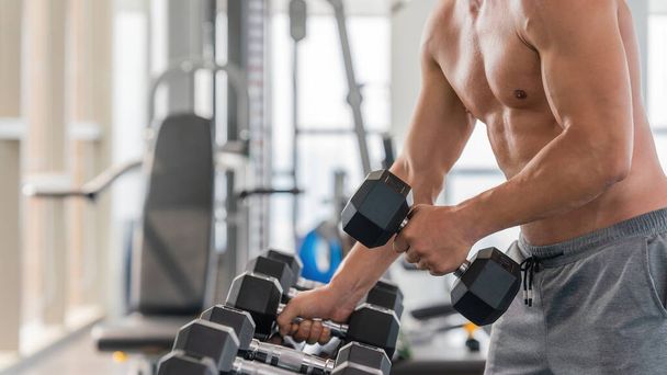 gym and fitness background of close up dumbbell with hand of athletic bodybuilder man lifting from dumbbell rack in gym and futness club - Foto, imagen
