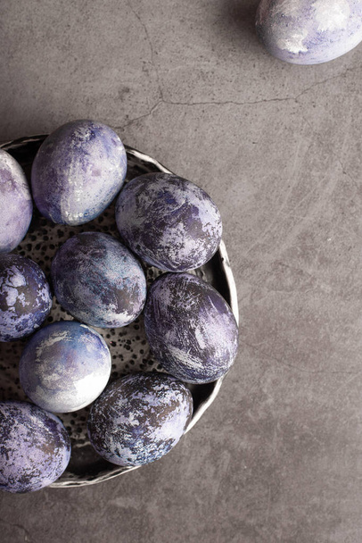 marble Easter eggs on a dark background, hand-painted with natural blueberries, lie in a clay cup on a stone table. Easter preparation concept. - Fotó, kép