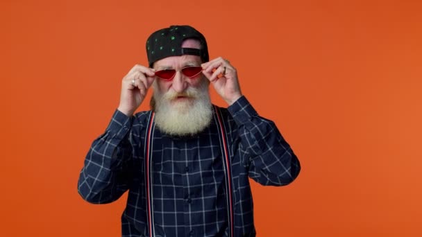 Verspielt glücklicher älterer bärtiger Mann mit Sonnenbrille und Schirmmütze blinzelt in die Kamera und lächelt - Filmmaterial, Video
