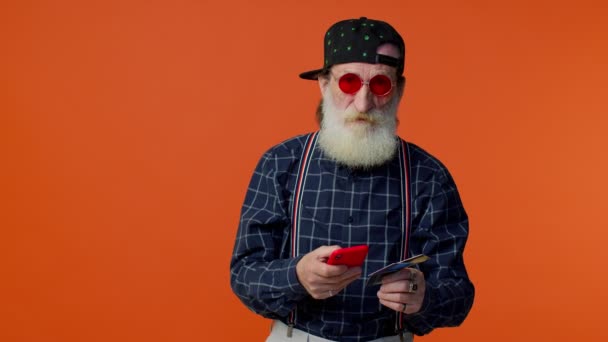 Senior old stylish bearded man using credit bank card and smartphone purchases online shopping - Footage, Video