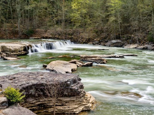 Valley Falls State Park near Fairmont West Virginia in the spring with the multiple waterfalls with cascading water flowing hard through the river and rocks with trees in the background. - Photo, Image
