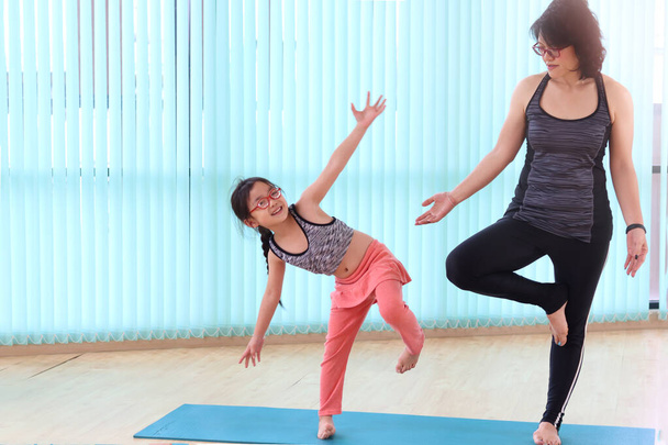 Mutter und Tochter machen gemeinsam Yoga im Indoor-Studio, die sportliche Familie praktiziert Yoga im Stehen und versucht es mit Baumhaltung, Workout und Übungen zur Körperpflege.. - Foto, Bild