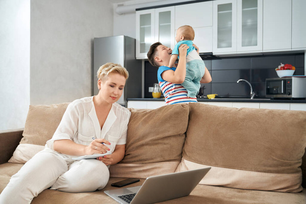 Pleasant woman working on laptop while sons playing together - Photo, Image