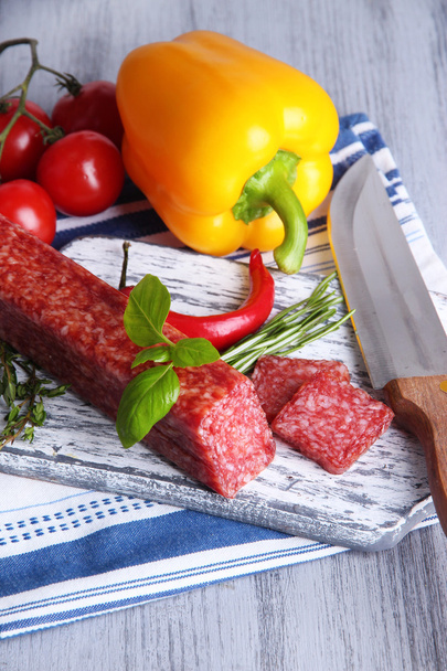 Tasty salami sausage, vegetables, knife and spices on wooden background - Foto, Bild