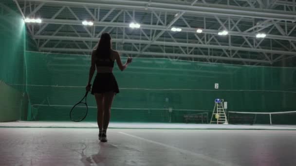 sexy kobieta na krytym korcie tenisowym, widok z tyłu smukłej pani w odzieży sportowej, trzymając rakietę tenisową - Materiał filmowy, wideo