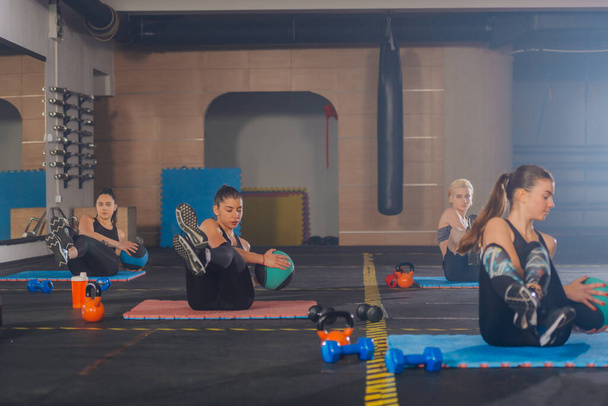 Chicas deportivas atractivas practicando ejercicios abdominales con pelota médica en un entrenamiento de fitness en grupo - Foto, imagen