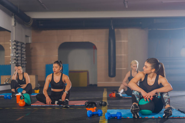 Filles sportives attrayantes se reposant de la pratique de l'exercice abdominal avec balle médicale dans un entraînement de fitness de groupe - Photo, image