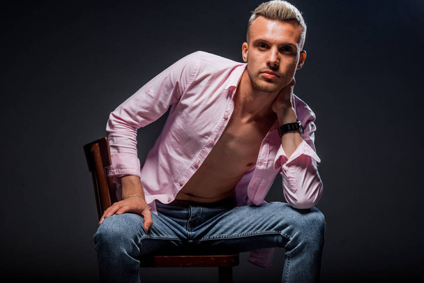 Cool young man dressed in light pink long sleeved shirt posing in dark studio - Fotoğraf, Görsel