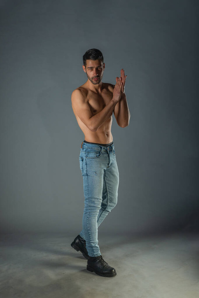 Full body portrait of sports man with denim jeans posing with bare torso in a dark studio - Фото, изображение