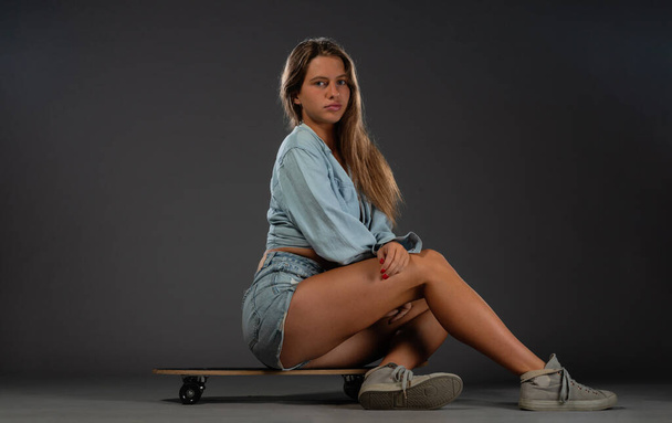 Приваблива дівчина позує зі своїм скейтбордом. Ізольована студійна фотографія на темному фоні
. - Фото, зображення