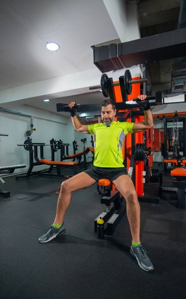 Forte atlético meia-idade homem exercício tríceps com barra no banco no ginásio - Foto, Imagem