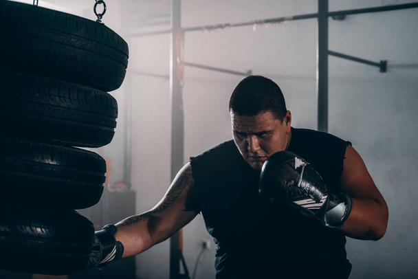 Przystojny muskularny mężczyzna w rękawiczkach bokserskich ćwiczy na oponach bokserskich podczas rozgrzewania - Zdjęcie, obraz