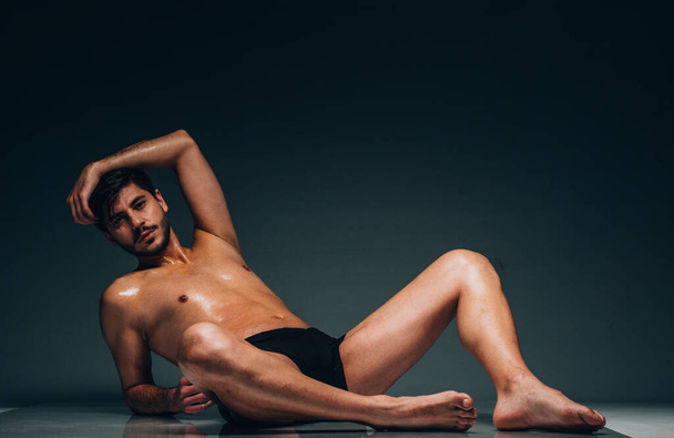 Satin perfection of skin. Confident young silhouette sportsman lying on floor in black underwear. He is showing his trained muscular body - Φωτογραφία, εικόνα