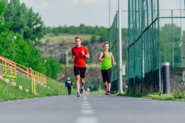 Mladí muži a ženy atleti běhají a běhají po silnici v parku - Fotografie, Obrázek