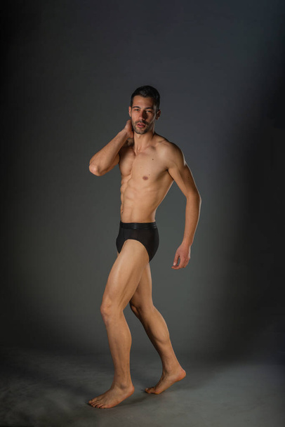 Сексуальный мужчина с мускулистым телом, позирующий голым с черными трусами в студии - Фото, изображение