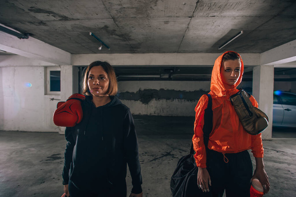 Két mosolygó női bokszoló portréja, amint egymás mellett állnak egy garázsban bokszkesztyűvel a kezükben. - Fotó, kép