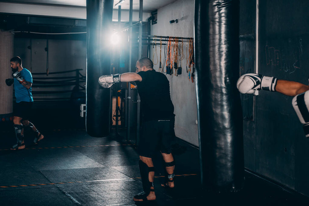 Siluet erkek boksör boks stüdyosunda büyük bir kum torbasına vuruyor. Erkek boksör sıkı çalışıyor. - Fotoğraf, Görsel