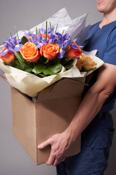 Corriere maschio bianco contenente una grande scatola con diversi mazzi di fiori. Concetto di consegna. - Foto, immagini