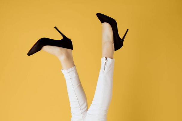 Kadınların ters bacakları ve siyah ayakkabıları. Beyaz kot, izole edilmiş sarı arka plan. - Fotoğraf, Görsel