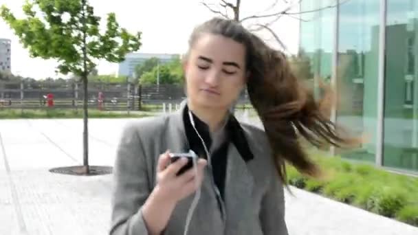Бізнес жінка йде і слухає музику на навушники до бізнесу будівлі - Кадри, відео