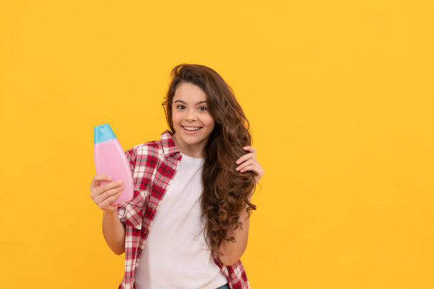 presenting cosmetic product. beauty. kid use shower gel. happy teen girl with shampoo bottle. shampooing hair in salon. child with conditioner. long curly hair. daily habits and personal care. - Photo, Image