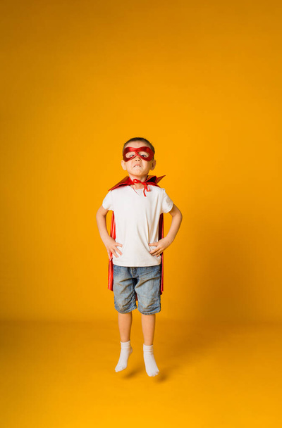 funny toddler boy in a hero costume is naughty on a yellow background with a place for text - Foto, Bild
