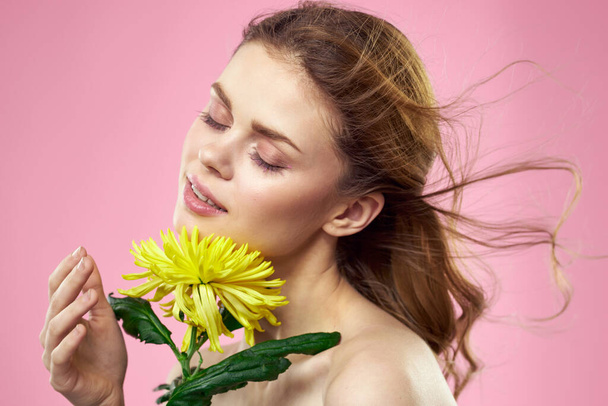 Menina bonita com uma flor amarela em um fundo rosa nua ombros maquiagem - Foto, Imagem