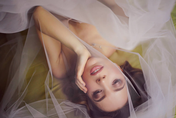 Beautiful bride in underwear on the bed covered with a veil. - 写真・画像