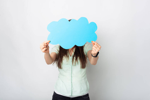 A photo of a woman holding with both hands in front of her a cloud shaped paper with free space in it near a white wall . - Fotoğraf, Görsel